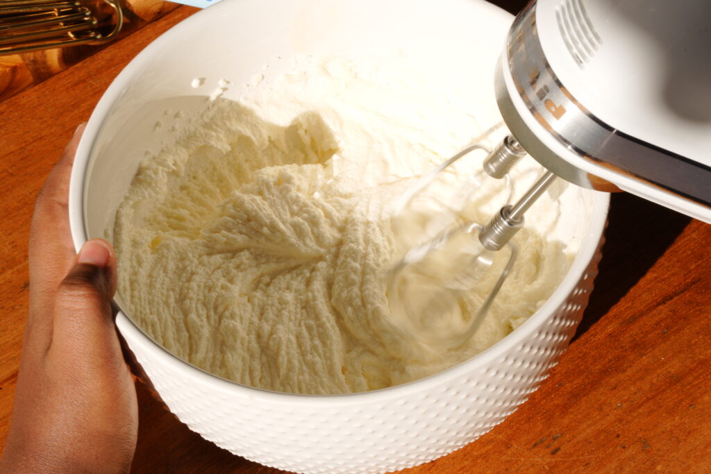 Mixing butter and sugar in a white bowl with a hand mixer to create a fluffy base for black cocoa cookie dough.