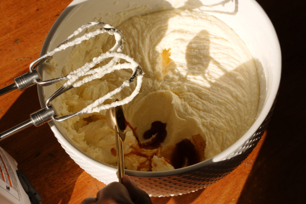 Pouring golden vanilla extract into creamed butter and sugar mixture before blending.