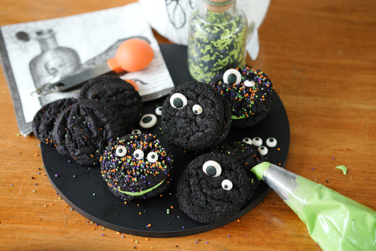 Black velvet cookie sandwiches filled with green buttercream and decorated with colorful Halloween sprinkles.