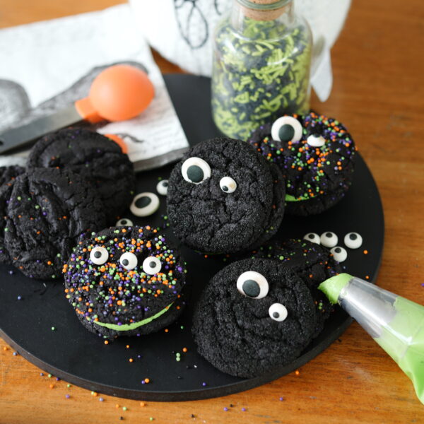 Black velvet cookie sandwiches filled with green buttercream and decorated with colorful Halloween sprinkles.
