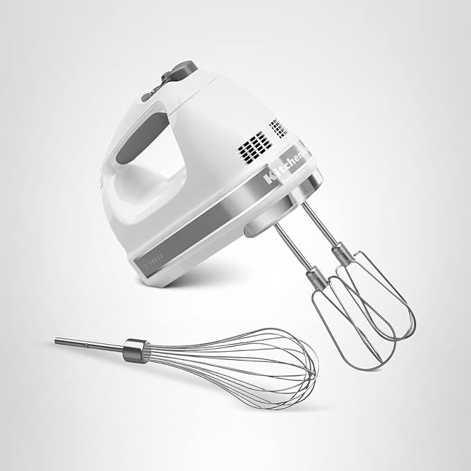white KitchenAid hand mixer with stainless steel beaters and whisk attachment on light background