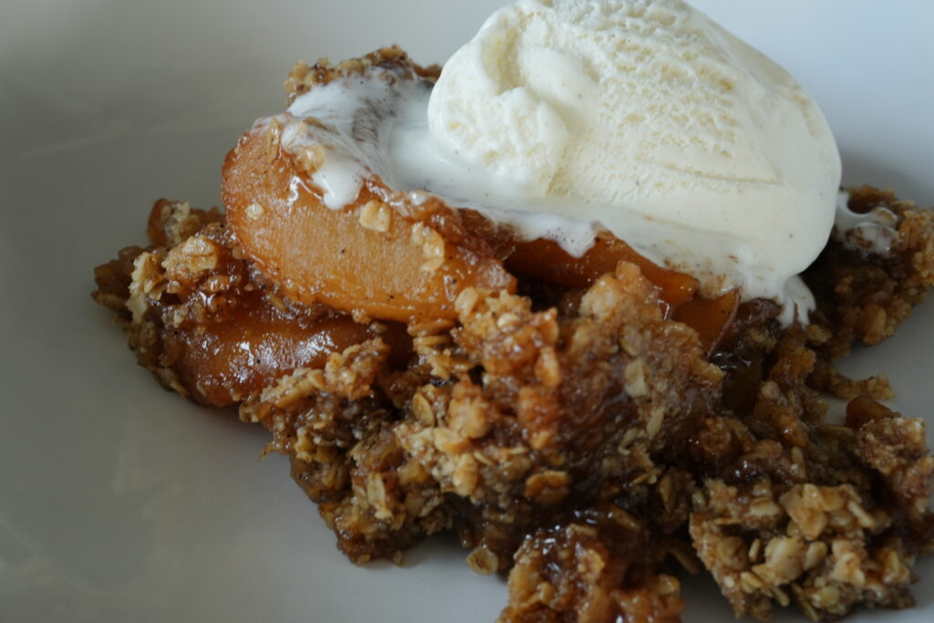 Close-up of homemade slow cooker apple crisp topped with a scoop of melting vanilla ice cream, featuring tender spiced apples and a golden oat topping.