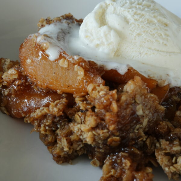 Close-up of homemade slow cooker apple crisp topped with a scoop of melting vanilla ice cream, featuring tender spiced apples and a golden oat topping.
