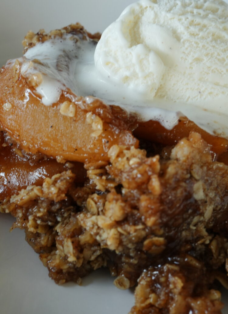 Close-up of homemade slow cooker apple crisp topped with a scoop of melting vanilla ice cream, featuring tender spiced apples and a golden oat topping.