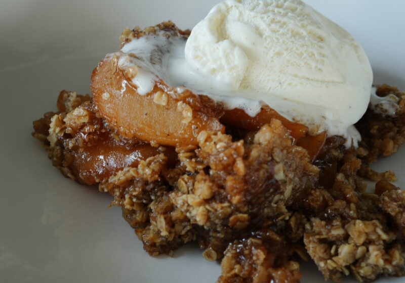 Close-up of homemade slow cooker apple crisp topped with a scoop of melting vanilla ice cream, featuring tender spiced apples and a golden oat topping.