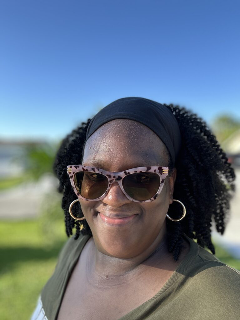 Homeschooling and working from home mom Shani Fay smiling after her morning walk, wearing sunglasses and a headband under a bright blue sky.