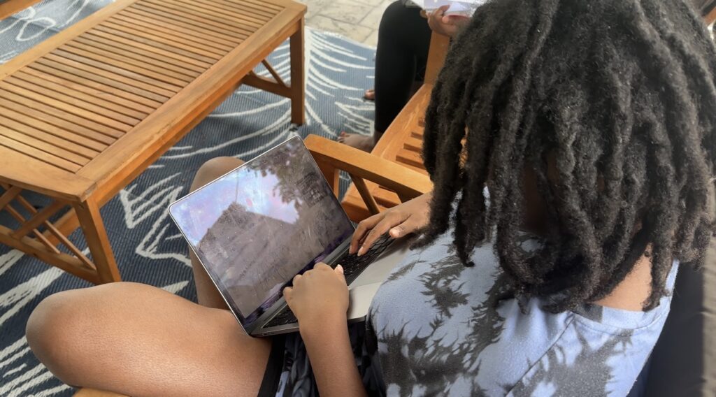 Teen homeschooling outdoors on a laptop while sitting on the patio, part of a working and homeschooling from home day.