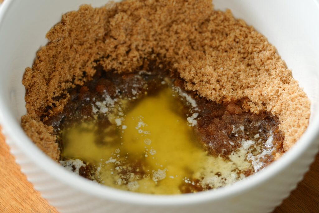 White bowl with melted butter poured over brown sugar and granulated sugar mixture to begin cookie dough for white chocolate chip blueberry pie cookies.