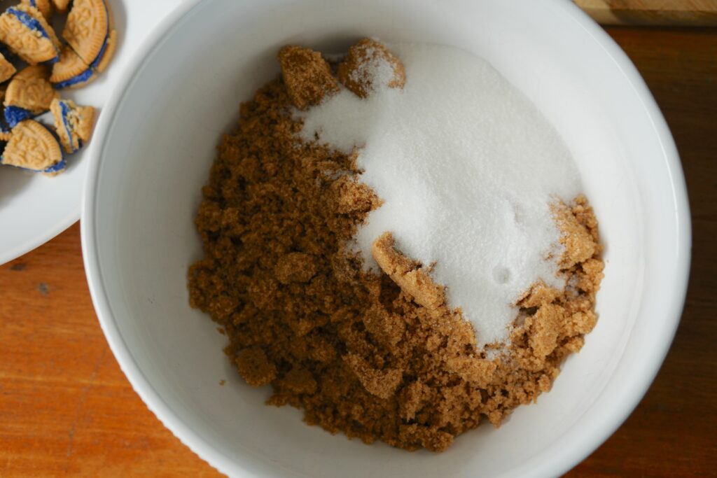 White bowl filled with brown sugar and white sugar before being combined for cookie dough.