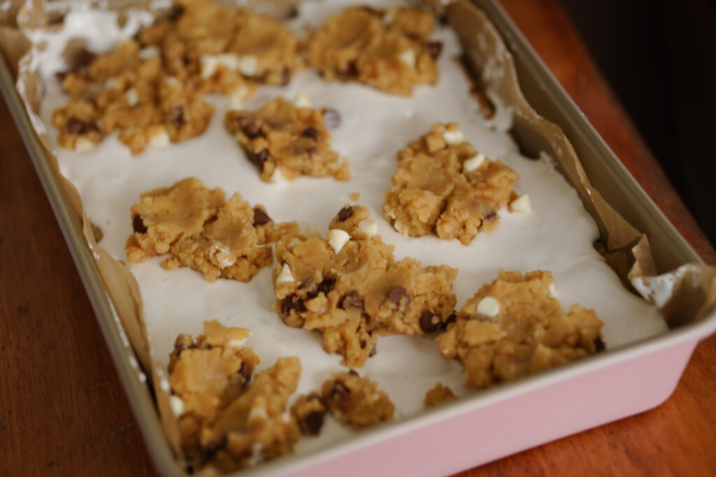 Small pieces of cookie dough placed on top of marshmallow layer in pan.