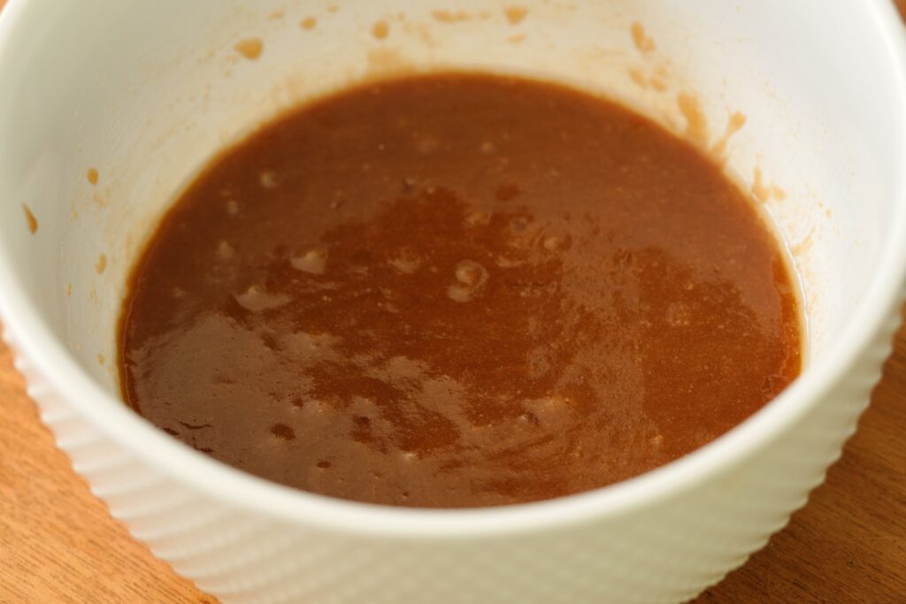 White mixing bowl with melted butter and sugars blended into a smooth base for cookie dough.