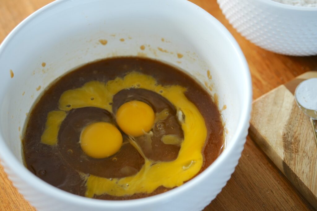 Two raw eggs sitting in a bowl of butter and sugar mixture for white chocolate chip blueberry pie cookies.
