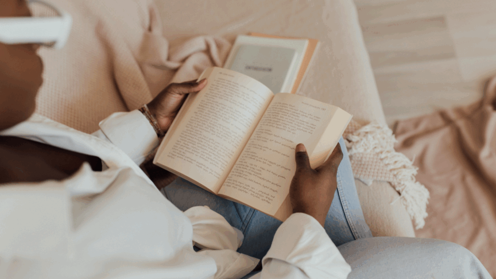 Black woman in a white blouse sitting on a cozy couch reading a book, representing calm and intentional morning boundaries for busy moms.