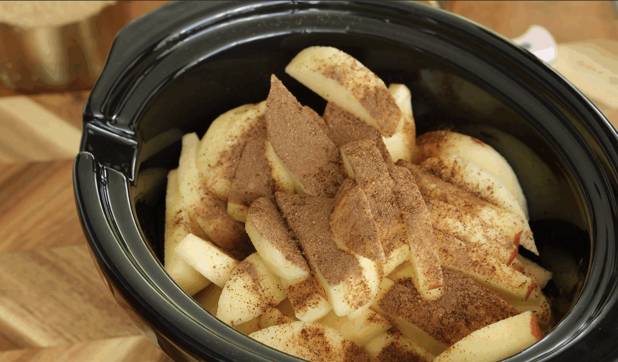 Peeled and sliced apples coated with cinnamon and spices in a slow cooker for apple crisp.