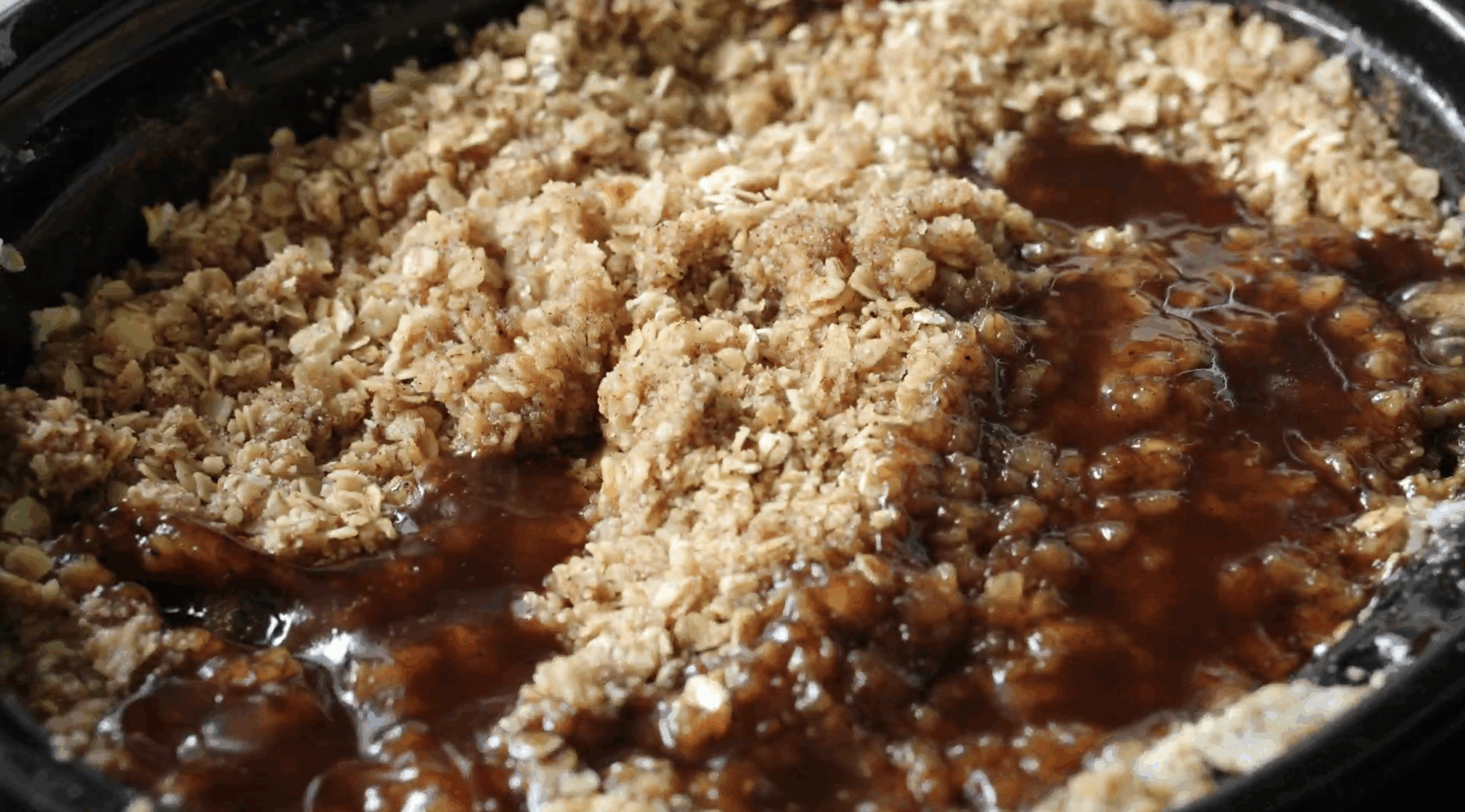 Oatmeal crumble topping layered over apple filling in a slow cooker before baking into apple crisp.