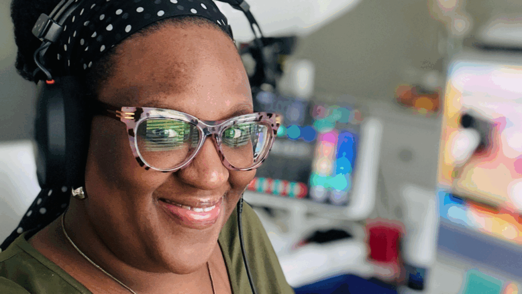 Woman smiling in her home office with headphones and computer setup, representing homeschooling teens while running a business.