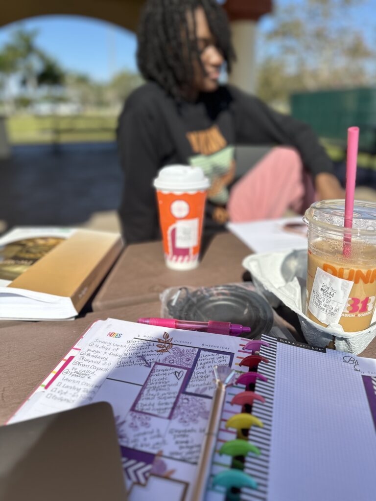 Open Happy Planner filled with homeschool notes, iced coffee, and supplies on a picnic table.