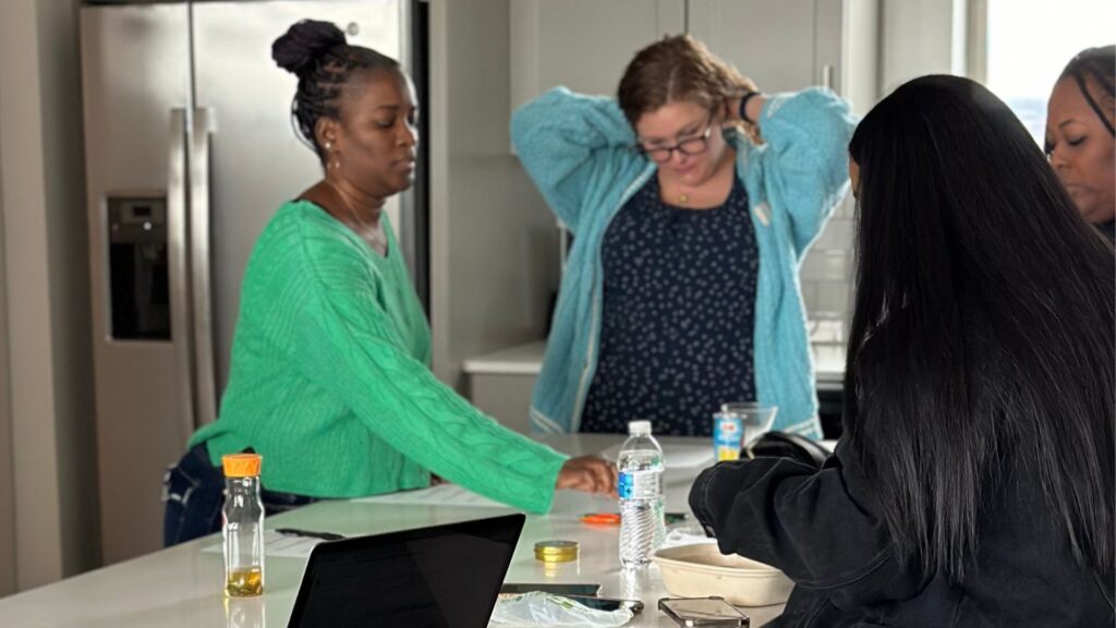 Executive team members collaborating in a kitchen space, woman in green sweater gesturing while others prepare for production