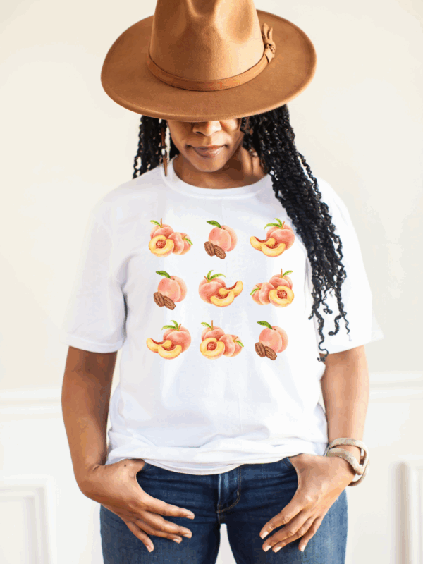 Woman in white Peachy Vibes graphic tee with peach illustrations, styled with hat.