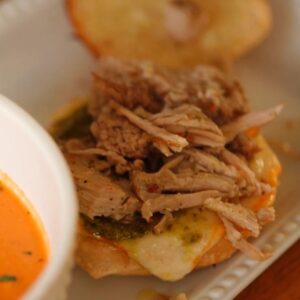 White bowl of creamy crock pot tomato soup served alongside a jerk pork grilled cheese sandwich.