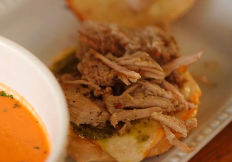 White bowl of creamy crock pot tomato soup served alongside a jerk pork grilled cheese sandwich.