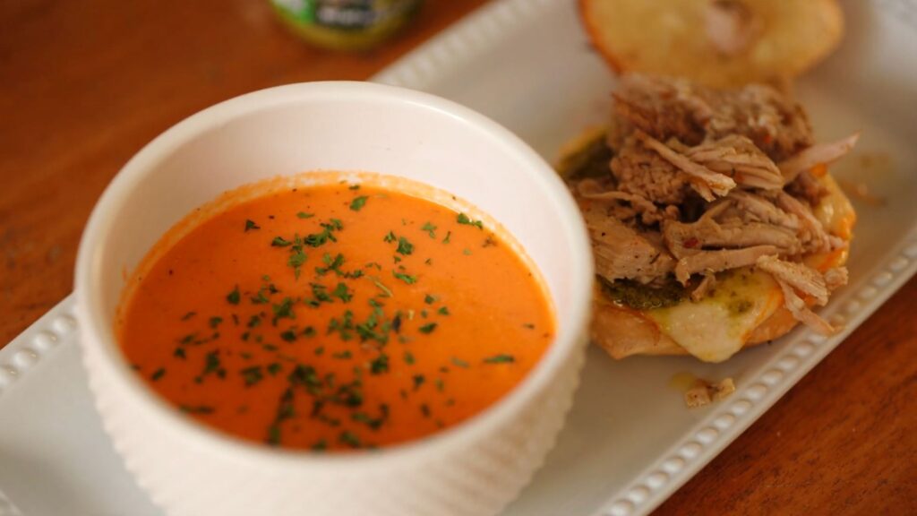 Shredded jerk pork piled onto cheesy bread next to a bowl of creamy crock pot tomato soup.