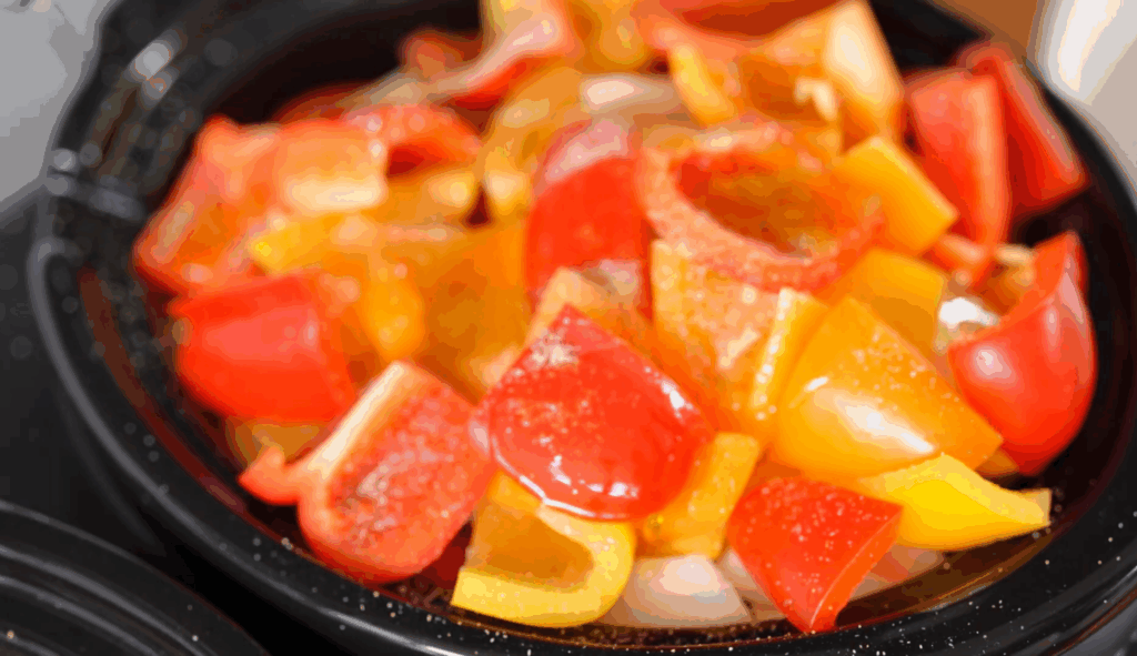 Chopped red, yellow, and orange peppers with tomatoes and seasoning in a crock pot for tomato soup.