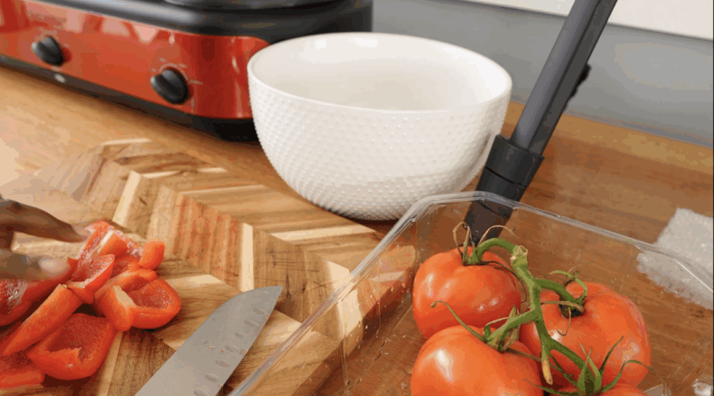 Hand arranging sliced red bell peppers on a wooden cutting board for creamy crock pot tomato soup.
