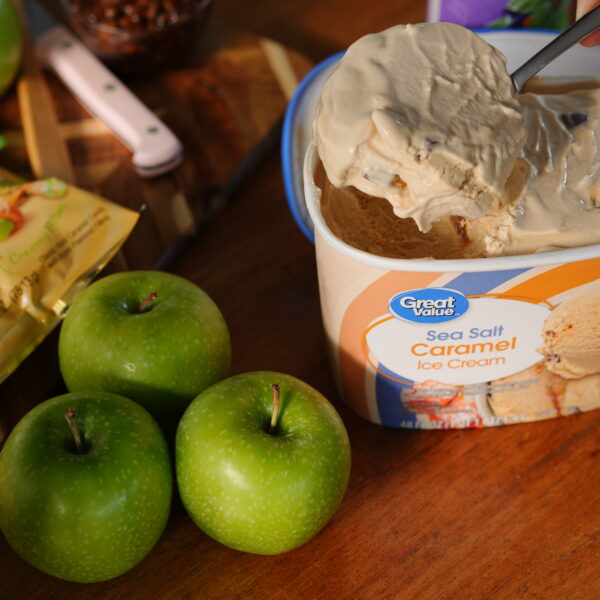 A spoon scooping creamy Great Value Sea Salt Caramel Ice Cream beside fresh green apples and caramel apple candy bars, ready to blend into a fall milkshake.